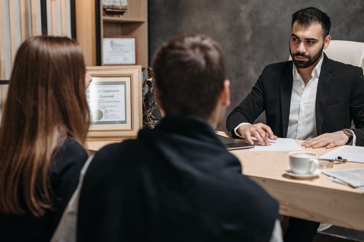 A legal professional meeting with clients across a desk covered in documents in a law office